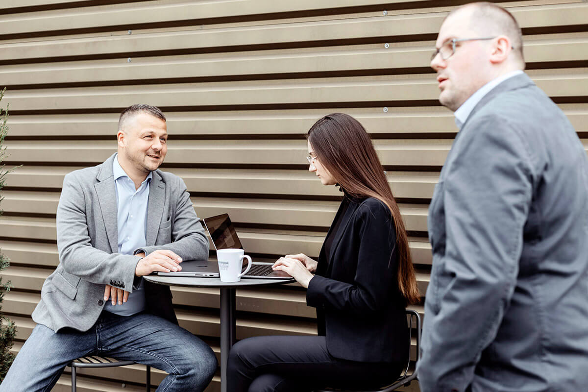 Three Bdat. colleagues in a discussion at an outdoor table with a laptop